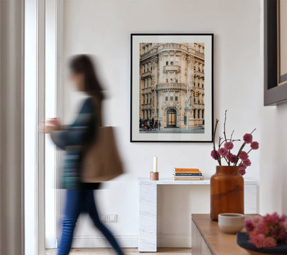 A blurred person walks by the Alwyn Court console table with vases, books, and a framed building photo.