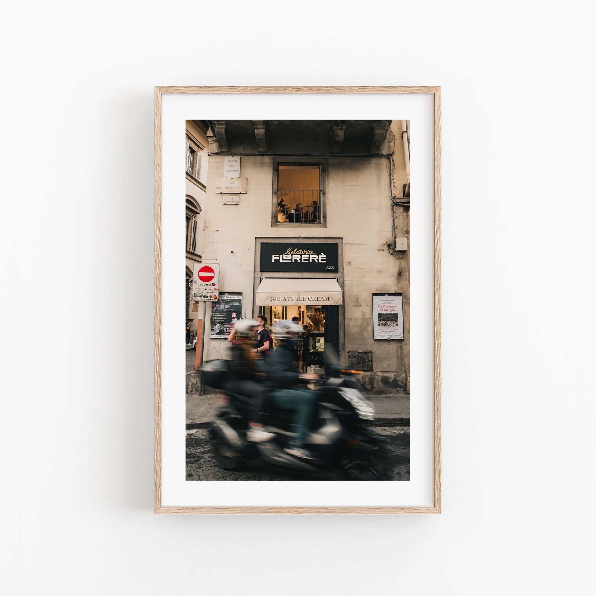 Framed photo of a Florence Motorcycle passing by a gelato shop entrance with people outside.