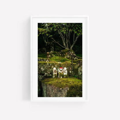 Framed photo: Three Wise Ones depicts two stone statues in red hats on a mossy rock amidst trees.