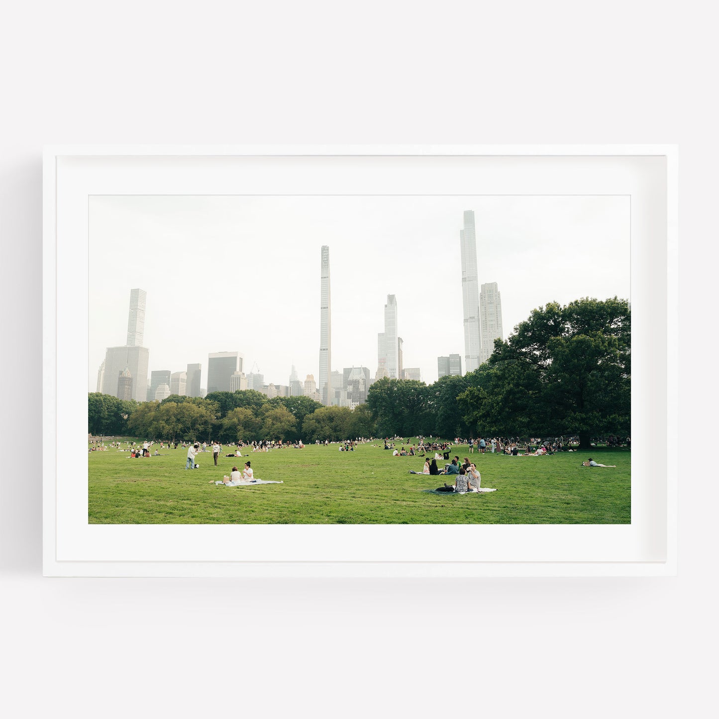 People relaxing on the Great Lawn, a grassy park with city skyscrapers in the background under a hazy sky.