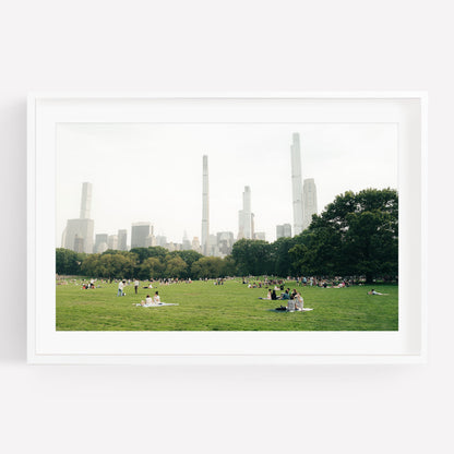 People relaxing on the Great Lawn, a grassy park with city skyscrapers in the background under a hazy sky.