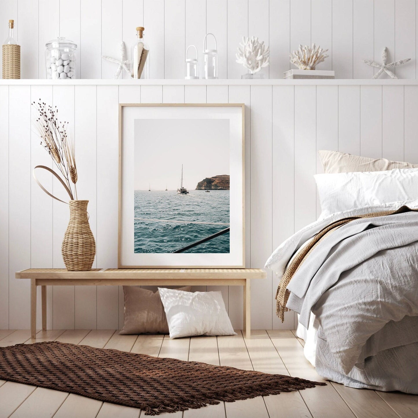 Seaside-themed bedroom with a framed Afternoon Sail I ocean photo, wicker vase, and white bedding on a wooden bench.