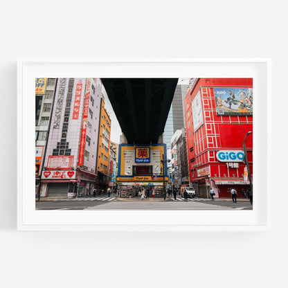 Akihabara scene with vibrant buildings, an overhead bridge, and people at a crosswalk in a Japanese city.