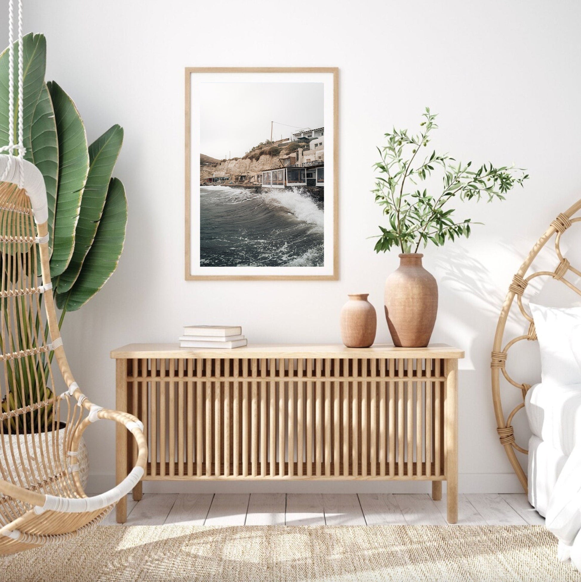 Minimalist room with wicker furniture, framed Akrotiri Wave photo, green plants, and natural light.