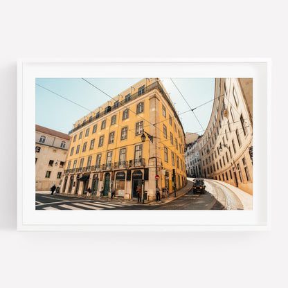 Framed photo of Baixa-Chiado: yellow building on curved street with people and tram tracks under a clear sky.