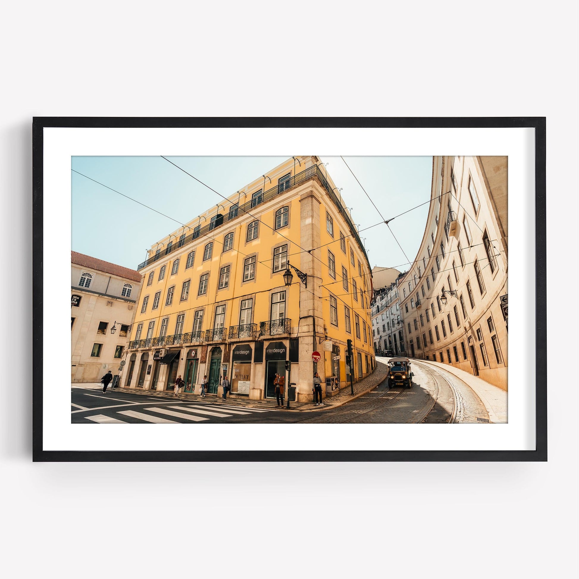 Framed photo of Baixa-Chiado: a yellow building on a curved street with tram tracks and pedestrians in Europe.