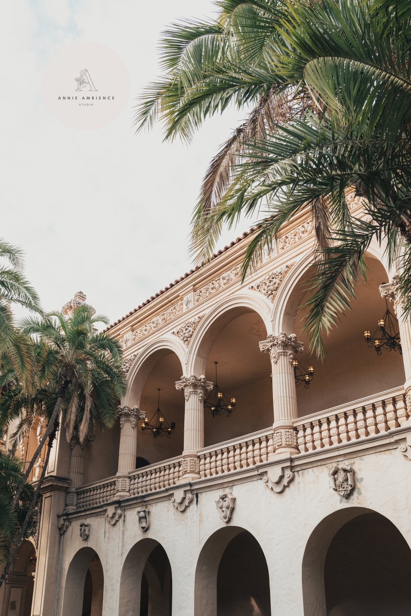 Balboa Architecture I: Elegant building with arched balconies and palm trees under a partly cloudy sky.