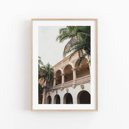 Balboa Architecture I: Framed photo of a historic building with arched balconies and palm trees on a cloudy day.