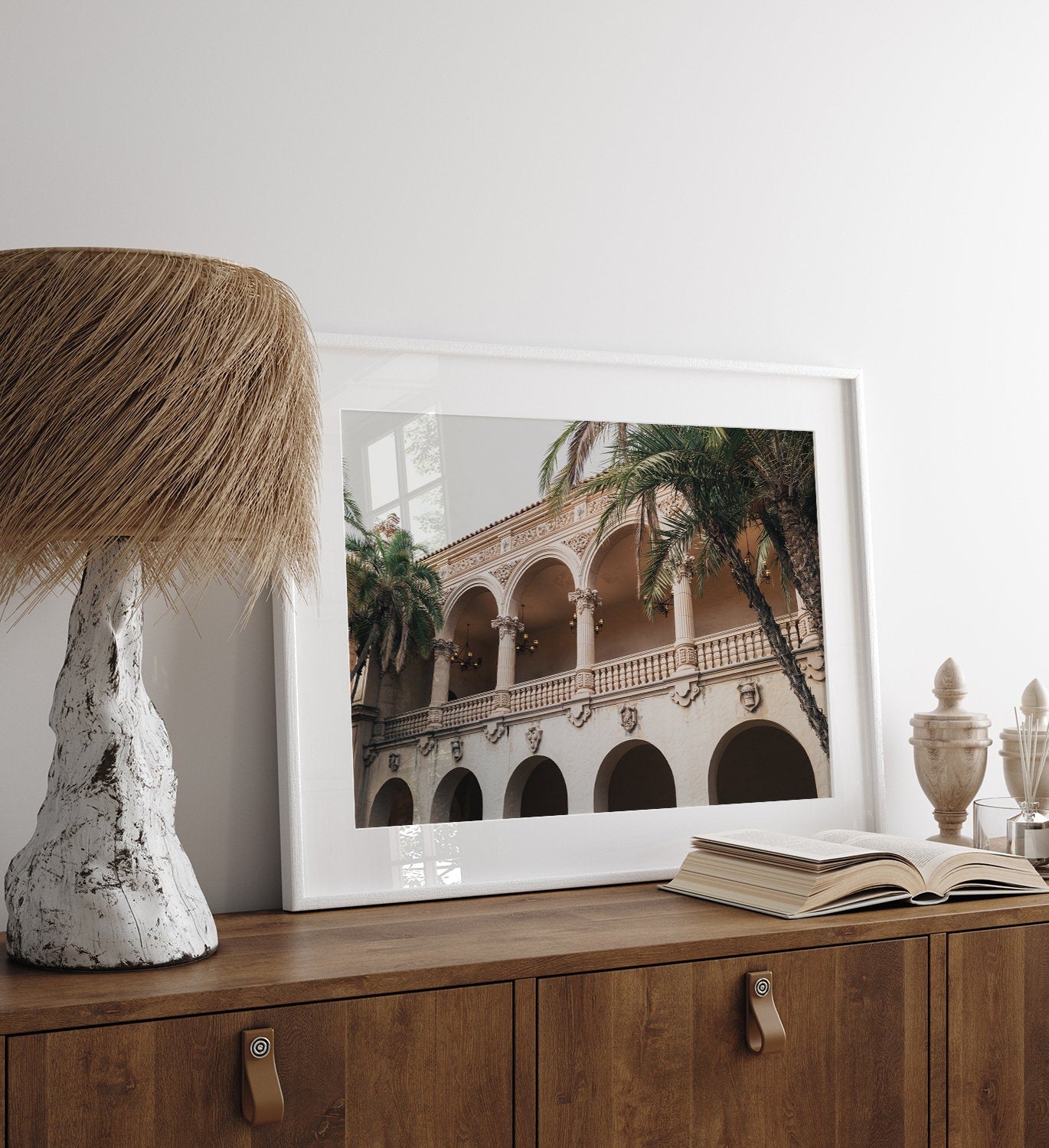 Balboa Architecture II, a framed photo of an ornate building, sits on a sideboard with a lamp and books.