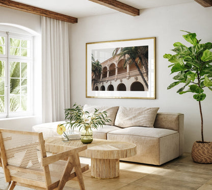 Minimalist living room with beige sofa, wooden table, green plant, and Balboa Architecture II print. Natural light filters in.