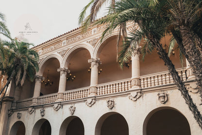 Balboa Architecture II: Ornate structure with arched balconies and detailed columns, surrounded by palm trees under clouds.