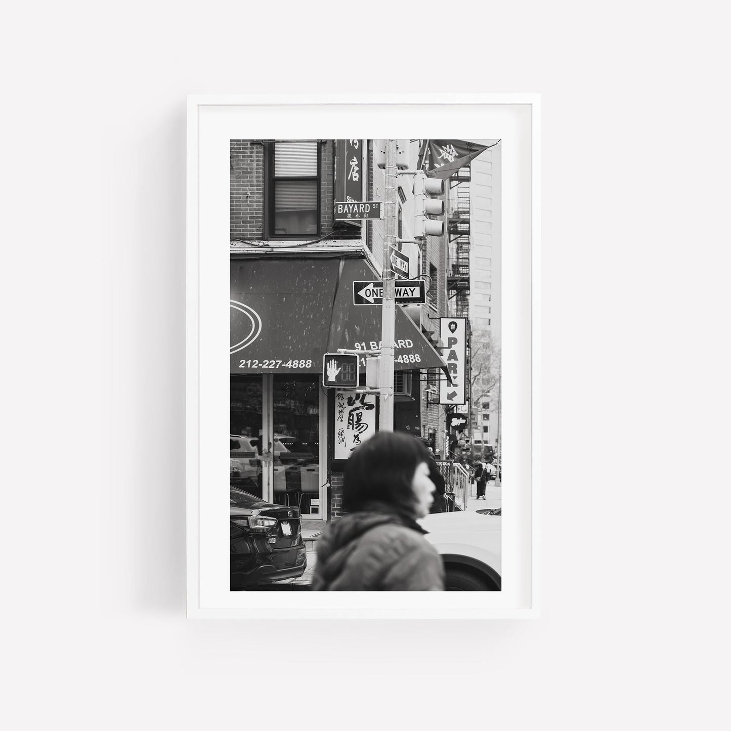 Bayard St. Black and White: A street scene with a person walking amid traffic and building signs.