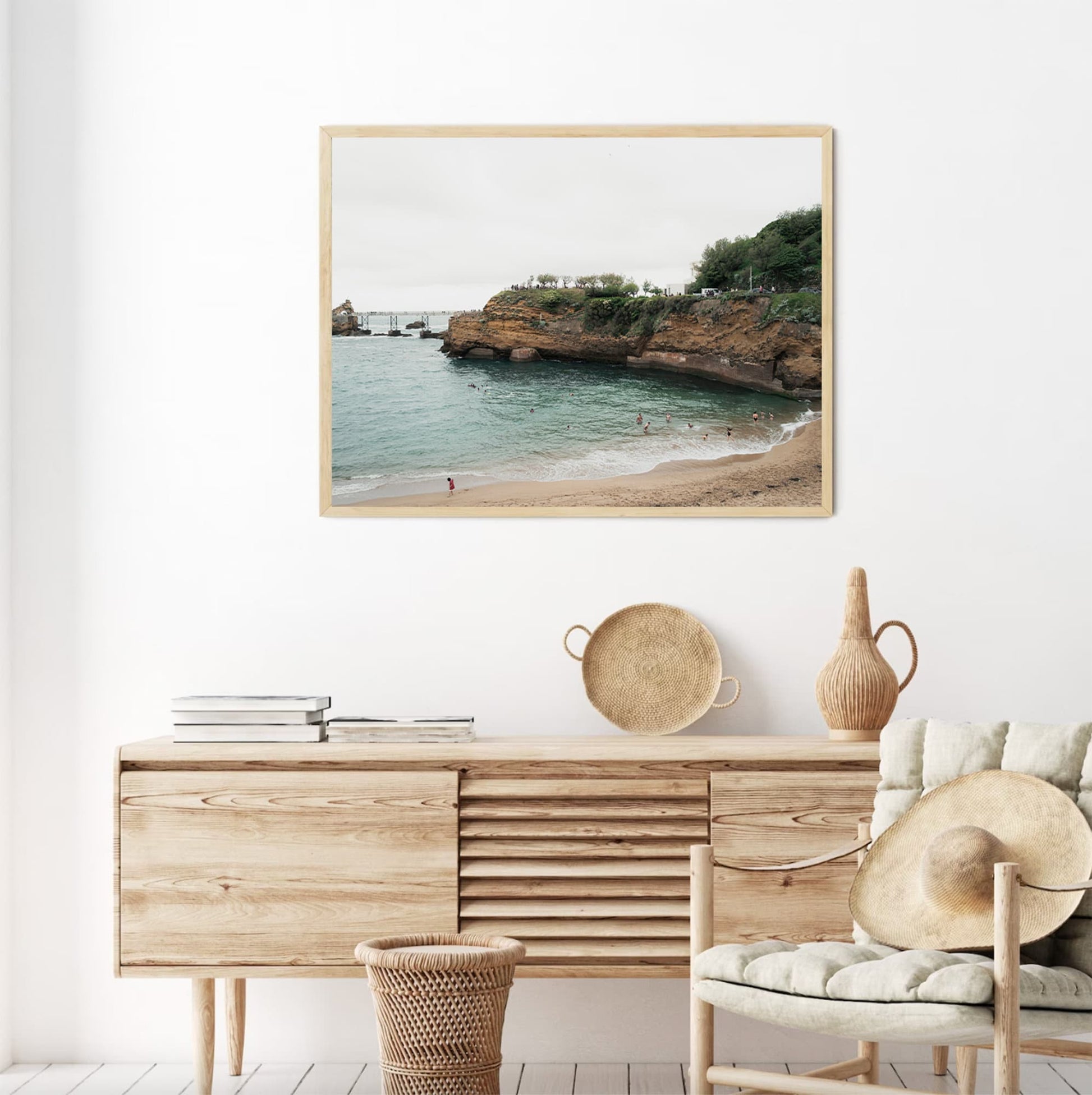 Biarritz Beach photo above a wooden console with decorative vases and a hat in a minimalist room.