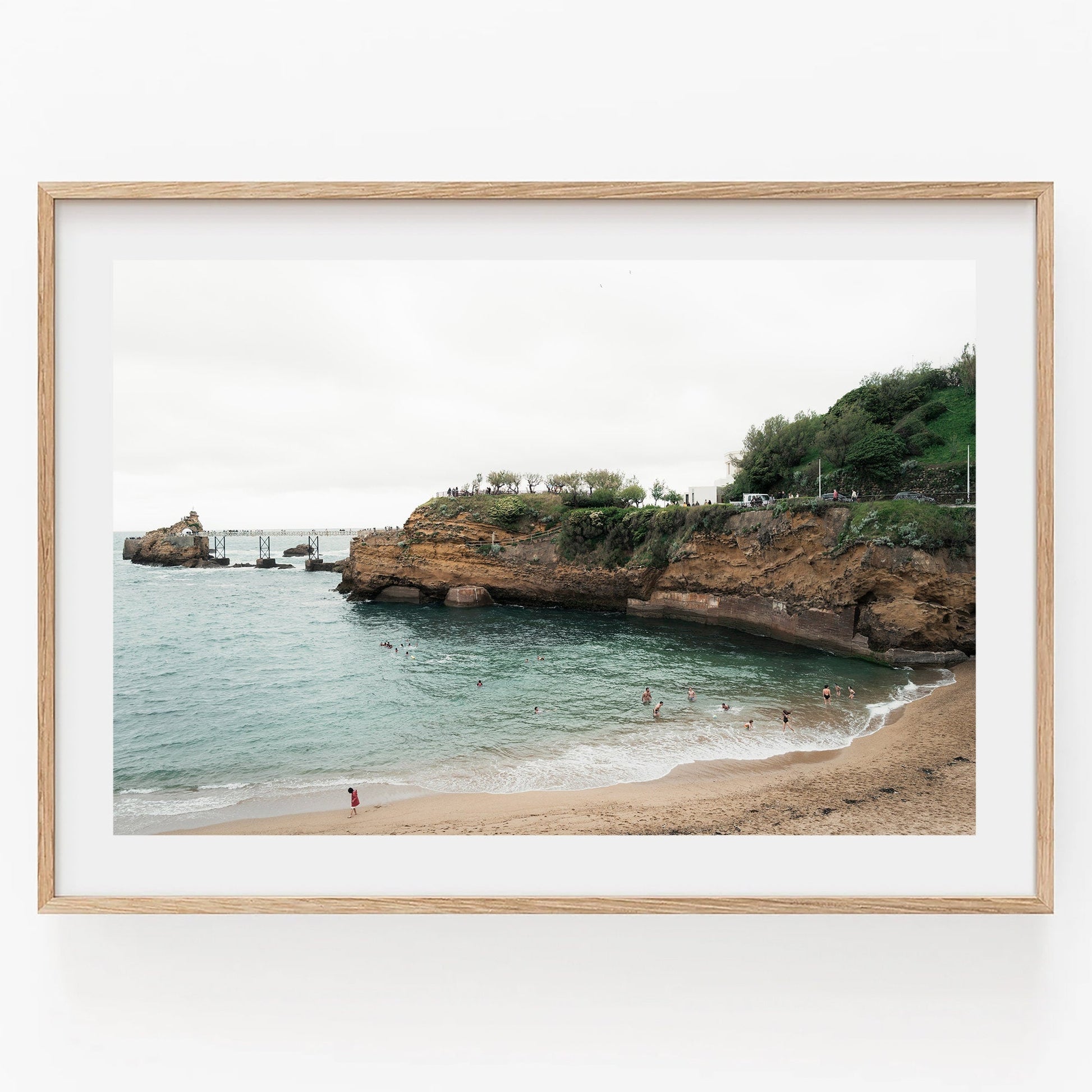 Framed photo of Biarritz Beach with swimmers and rocky cliffs in the background.