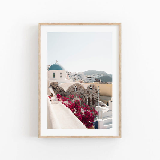 Framed Blue Dome photo of a Greek village with white buildings, blue-domed church, and pink flowers.