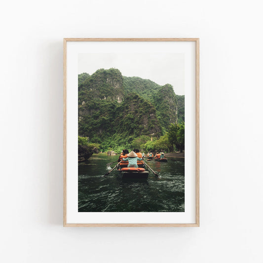 Framed Boat Row photo: people rowing on a river amid lush, green mountains.