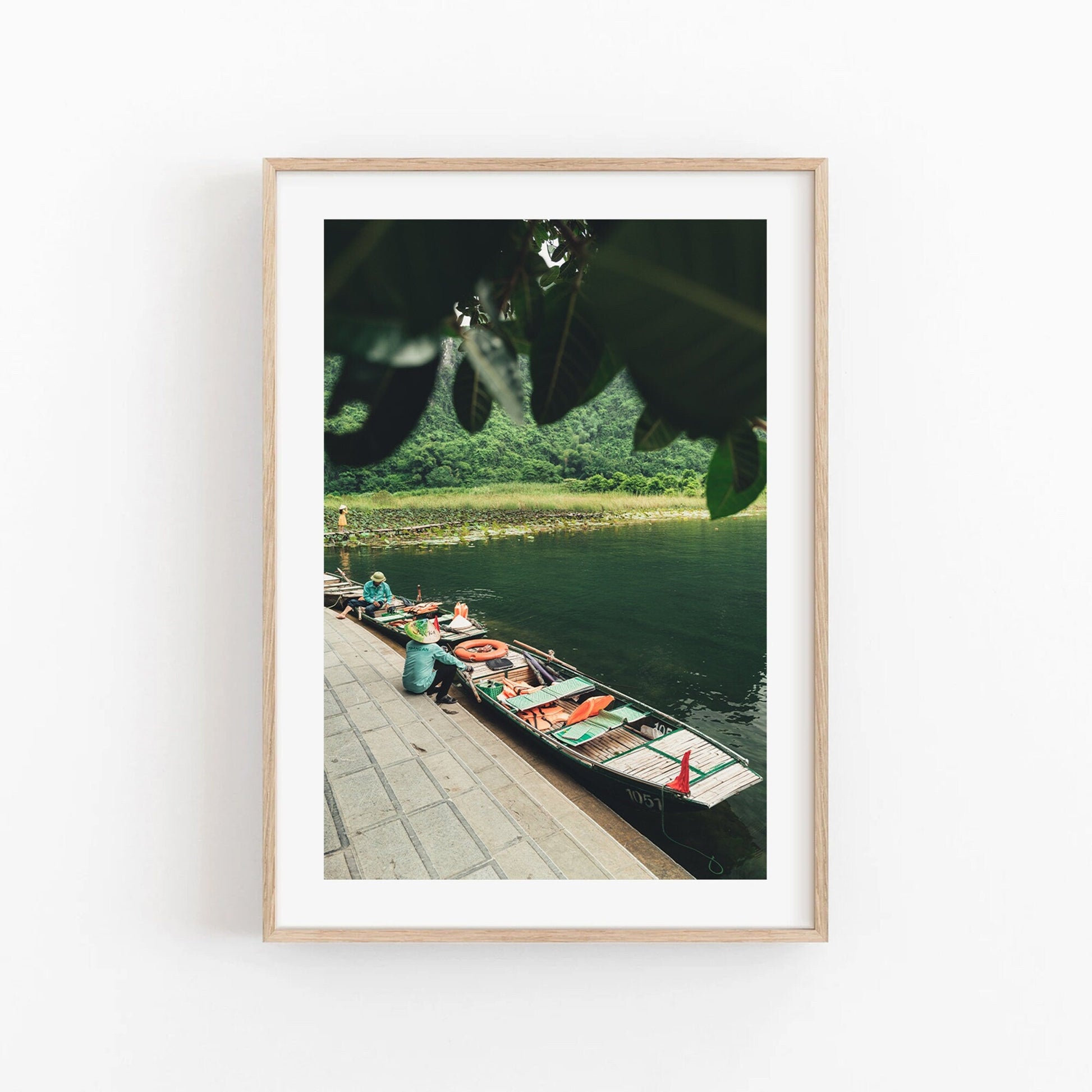 Framed photo titled Break Time: boats with people on a calm river, lush greenery, viewed from beneath tree leaves.