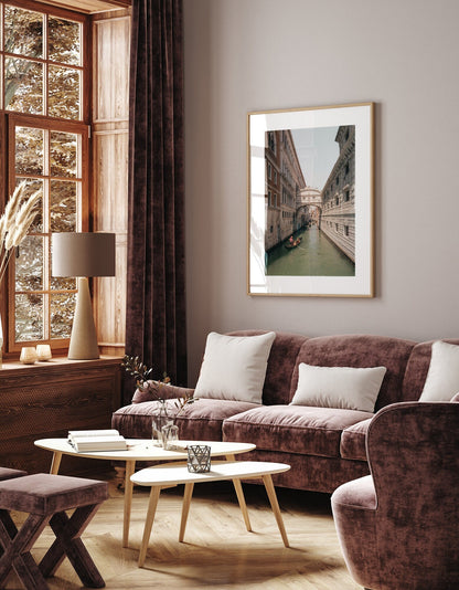 A cozy living room with plush furniture, a large window, and Bridge of Sighs framed above the sofa.