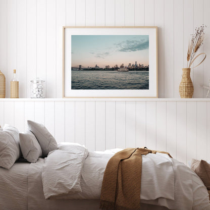 Cozy bedroom with Brooklyn Sunset framed above the bed, showcasing a cityscape of water, skyline, and soft lighting.