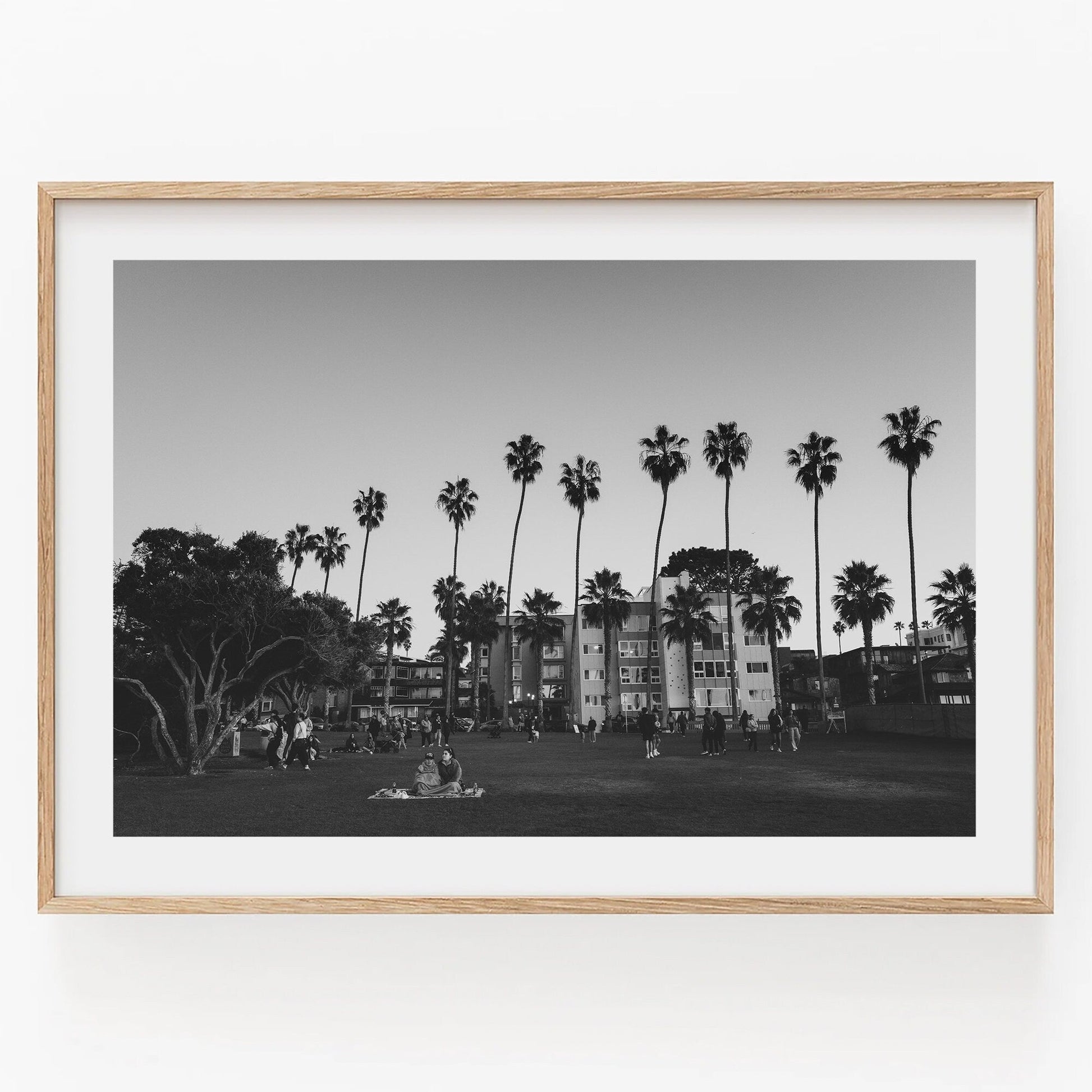 Black and white photo titled California Evening shows people relaxing on a grassy area with palm trees and buildings.