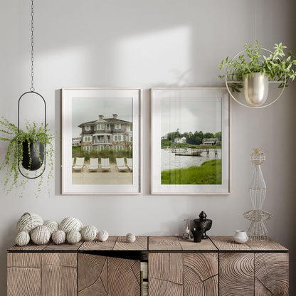 Modern interior featuring "Cape Cod - Set of 2" wall art of houses by water, hanging plants, and decorative accents.