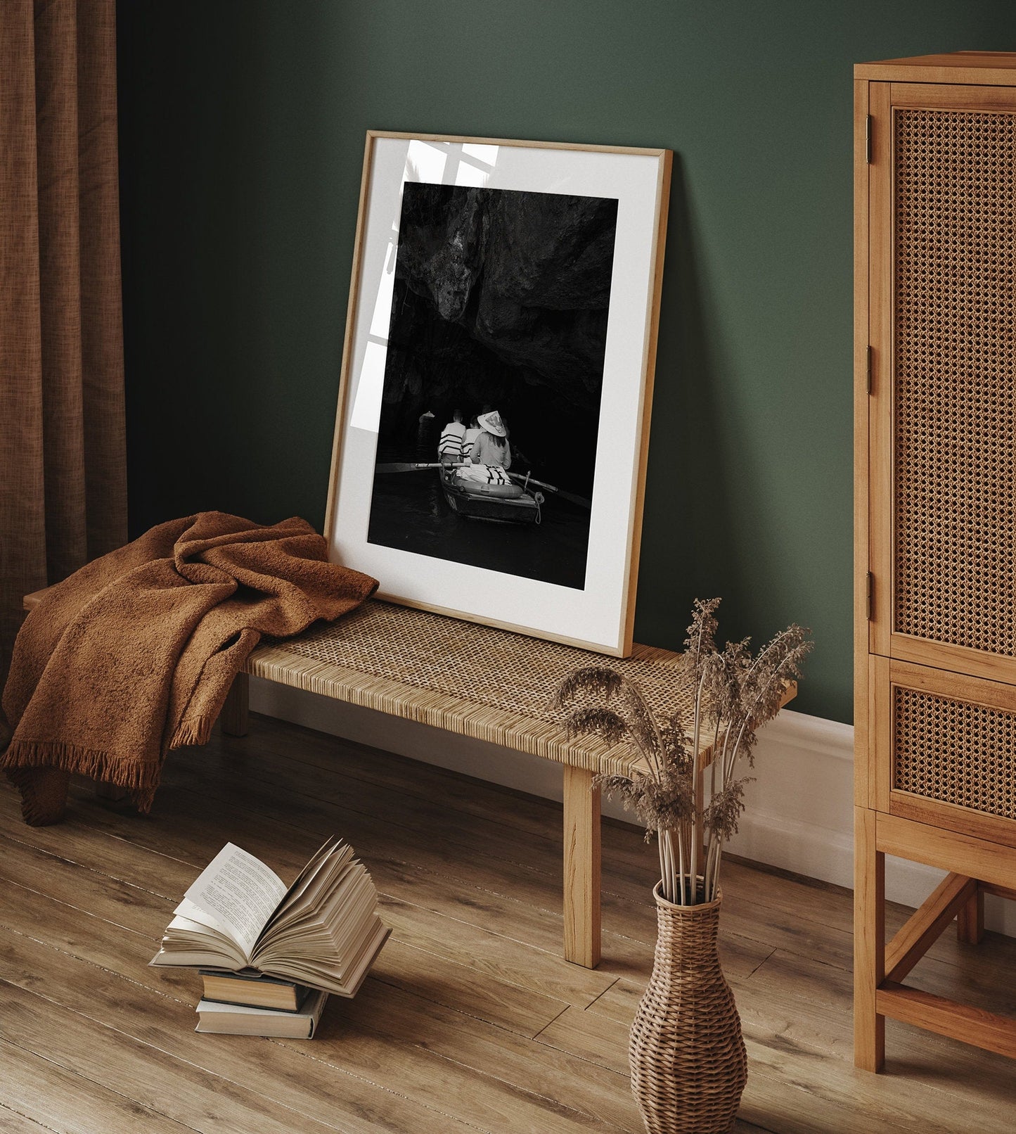 Cave Boat Black and White photo framed on a woven bench with an open book, vase of dried flowers, and a green wall backdrop.