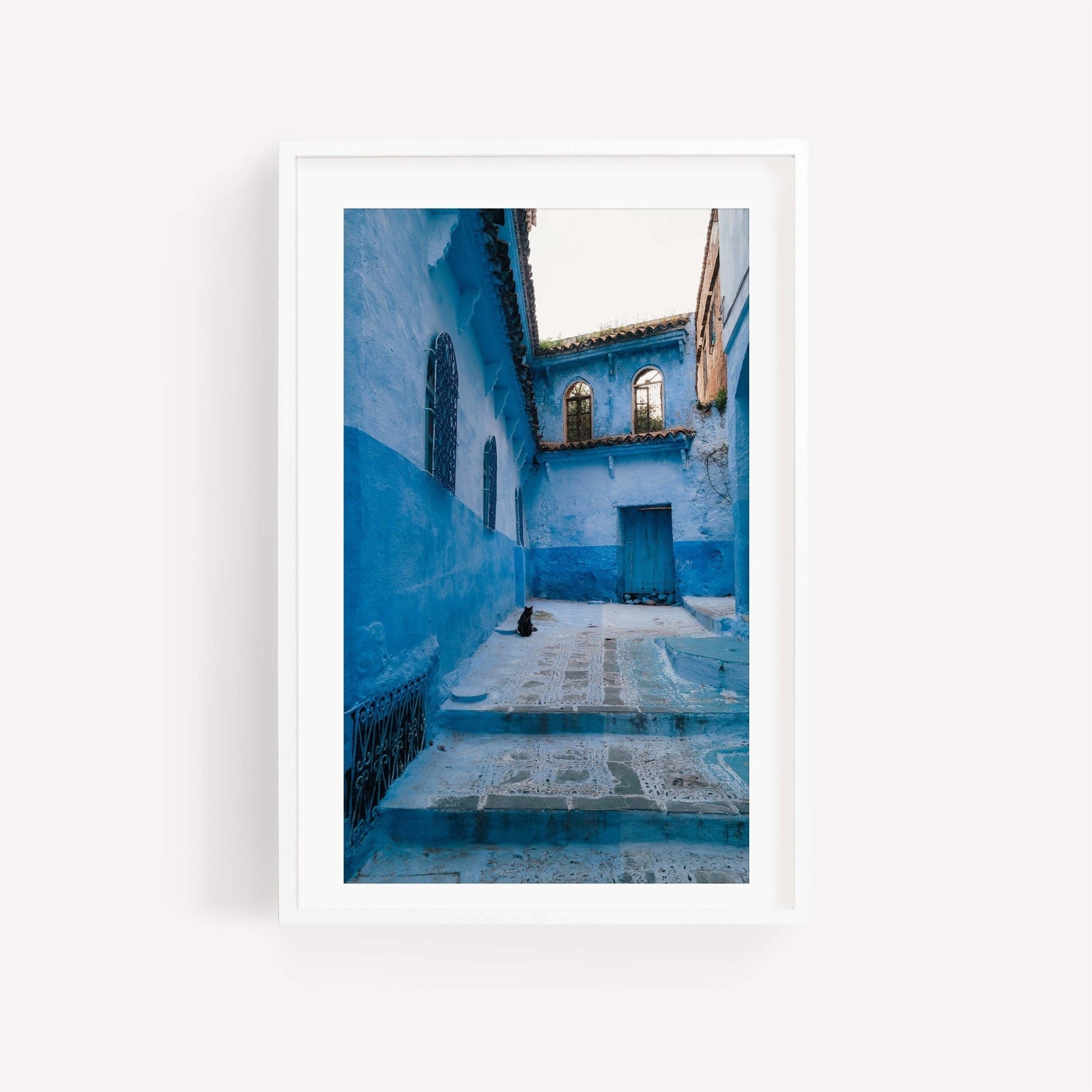 Framed photo titled Chefchaouen Cat featuring a black cat on steps in a narrow, blue alleyway.