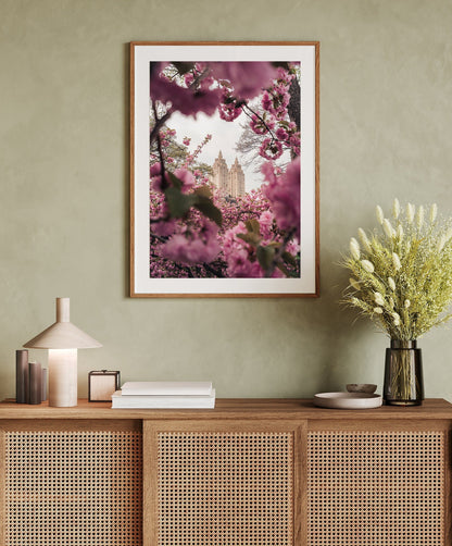 Cherry Blossom II on a green wall above a wooden sideboard with books, a lamp, and flowers.