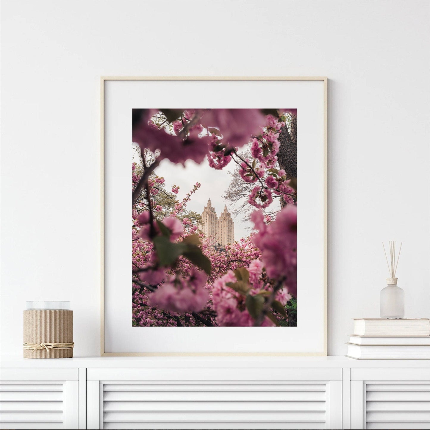 The Cherry Blossom II framed photo shows a building seen through pink blossoms, displayed on a white shelf with candles and a vase.