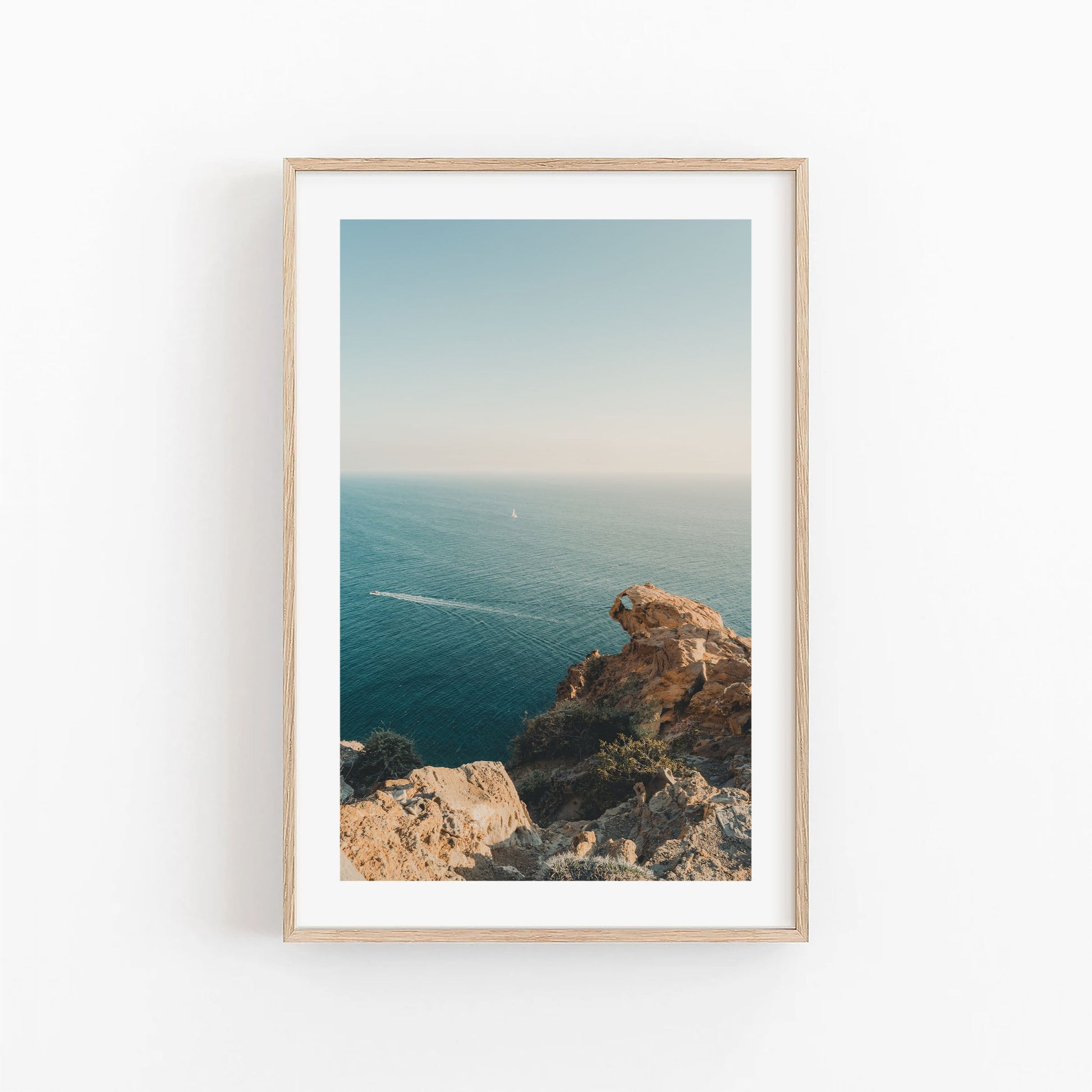 Cliffside Paradise: Framed photo of rocky cliffs above a calm blue ocean with sailboat and speedboat in view.