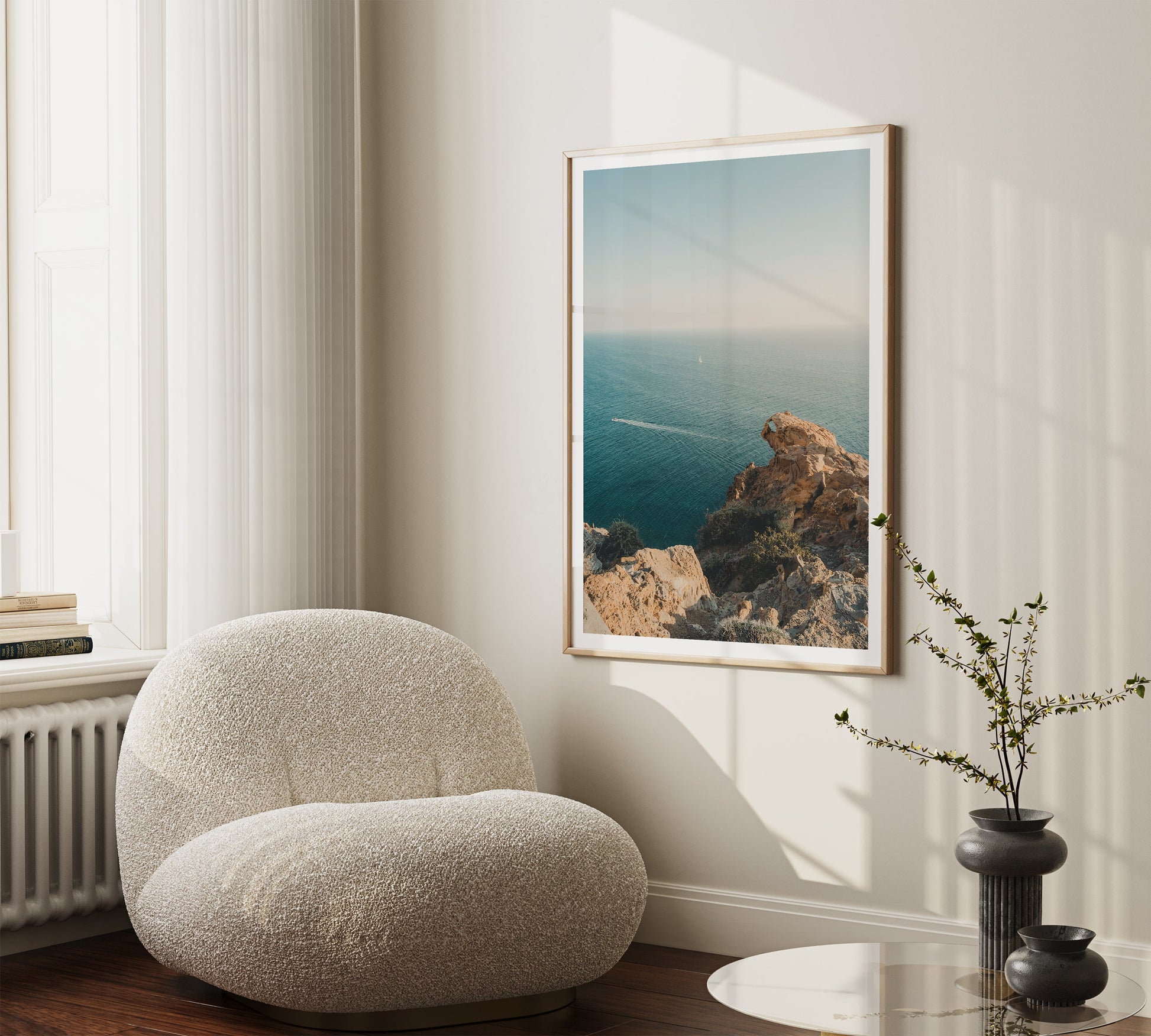 A cozy chair by the window, a framed Cliffside Paradise photo on the wall, and a vase with branches on the table.
