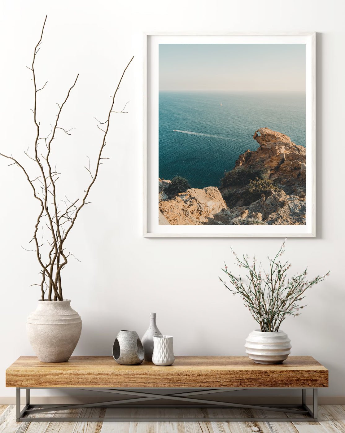 Minimalist wooden console table with vases beneath the framed Cliffside Paradise photo of rocky ocean cliffs.