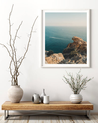 Minimalist wooden console table with vases beneath the framed Cliffside Paradise photo of rocky ocean cliffs.