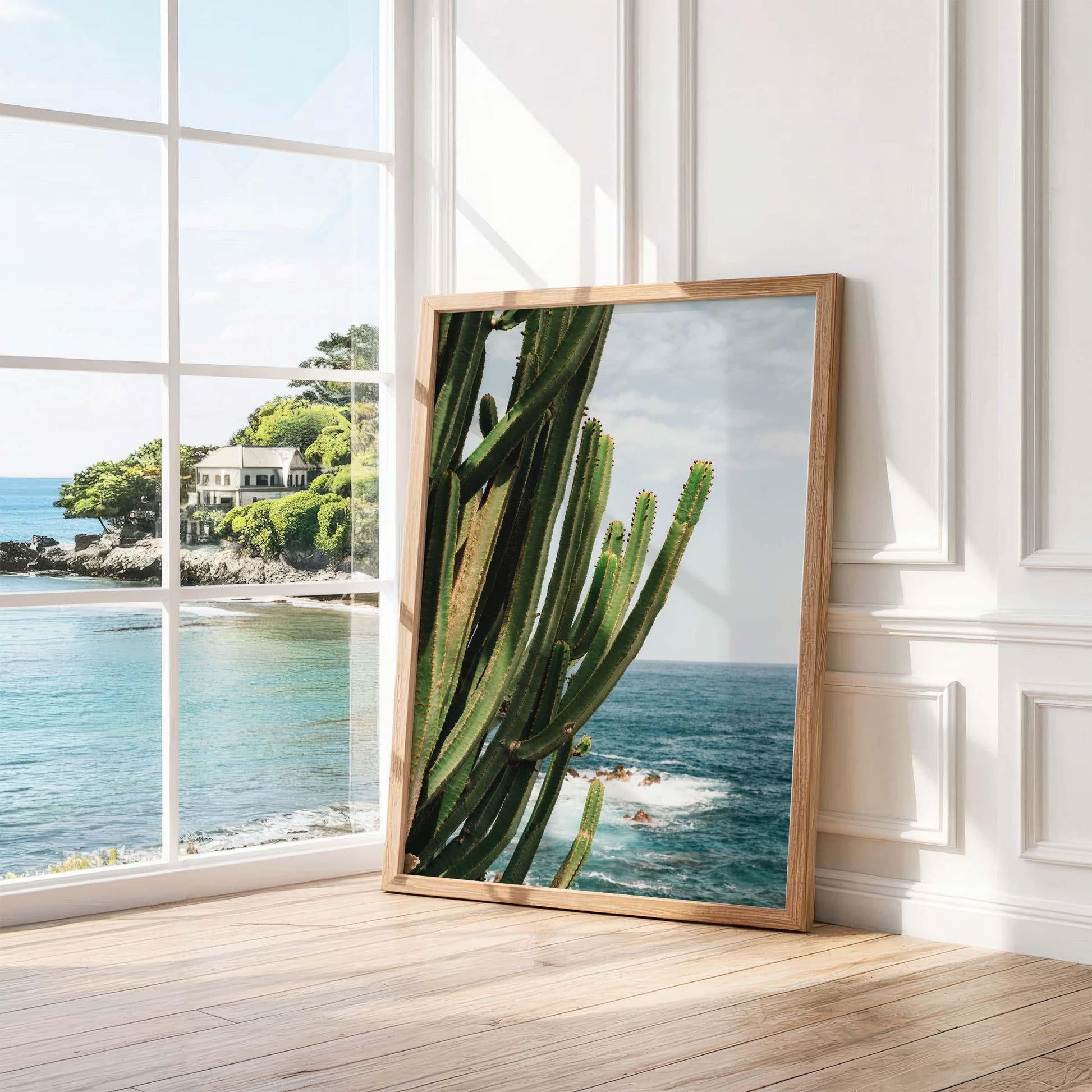 The Coastal Cactus framed photo sits by sunny sea-view windows, leaning against a white wall.