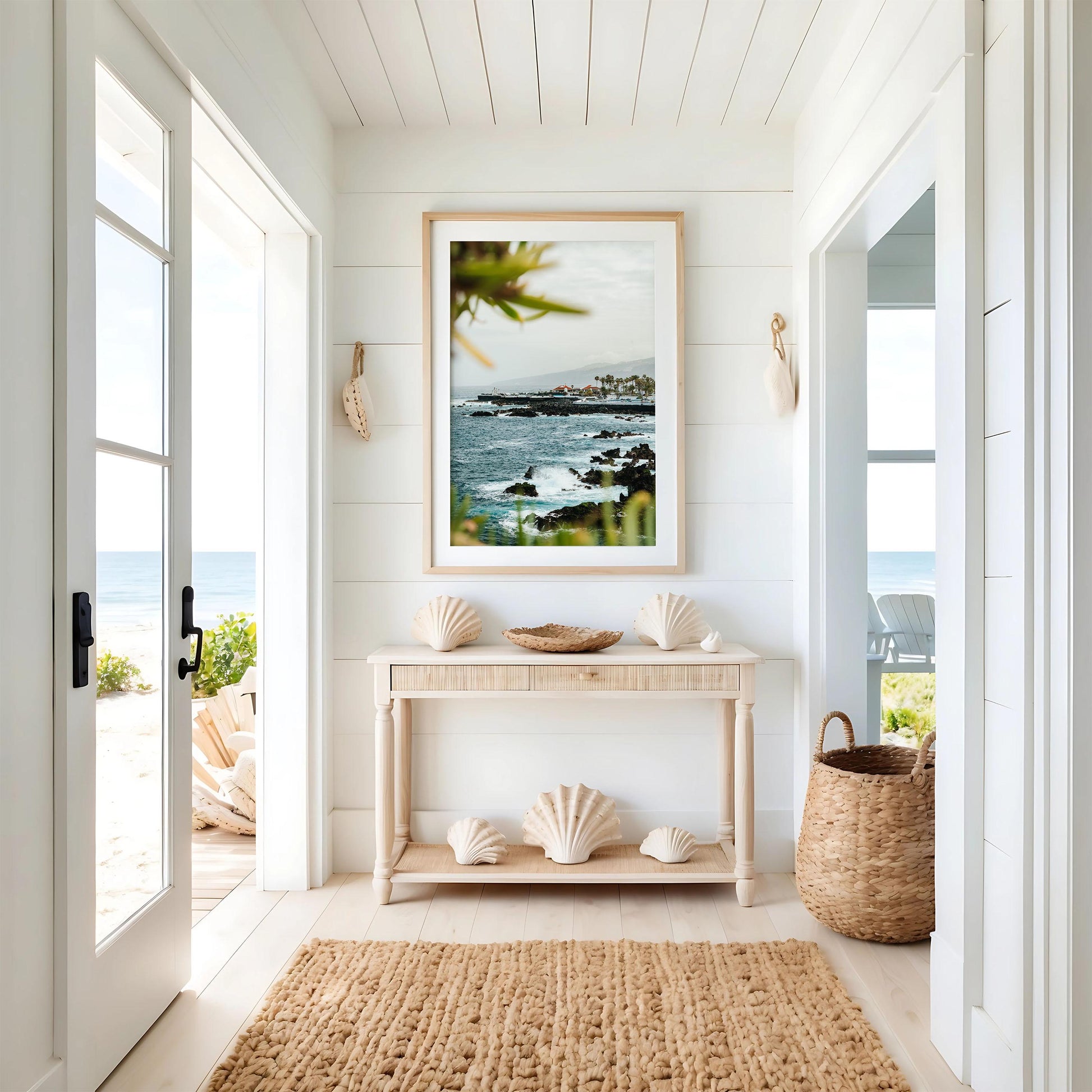 Coastal Glimpse: Bright hallway with coastal decor, woven rug, seashells, and framed ocean view leading to a beach patio.