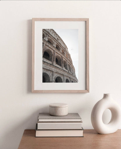 Colosseum II photo framed on a wall above a wooden table with books and a vase.