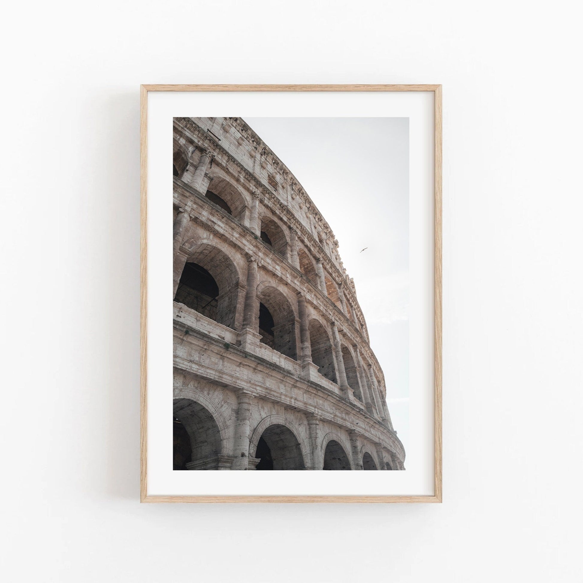 Colosseum II framed photo on a white wall, shot from a low angle with the Rome sky bright above.