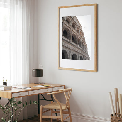 Colosseum II photo framed on wall above a wooden desk and chair, near a window with white curtains.