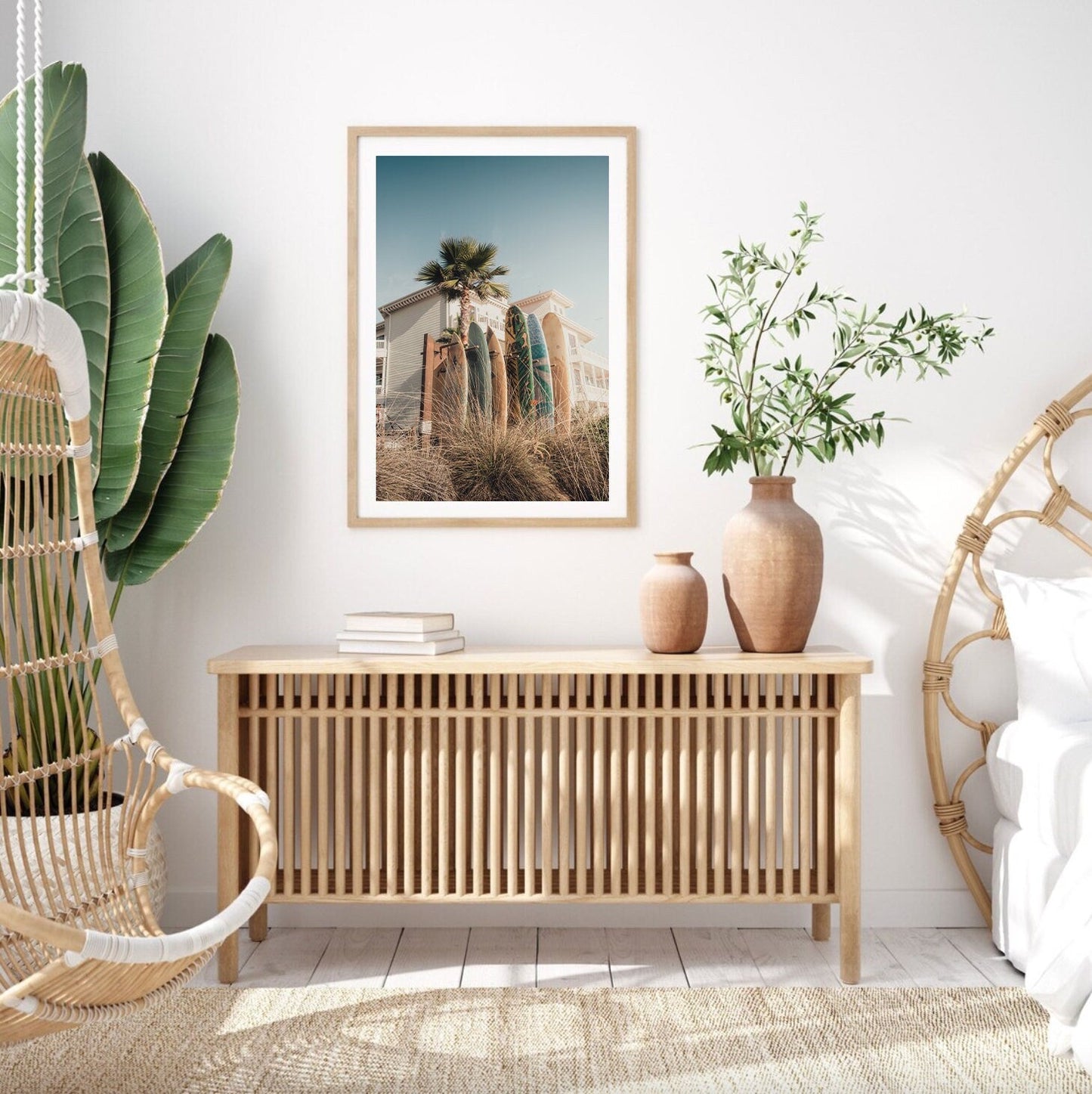 Minimalist living room with a hanging chair, wooden console, framed Coronado Surfboards photo, and big neutral-tone plants.