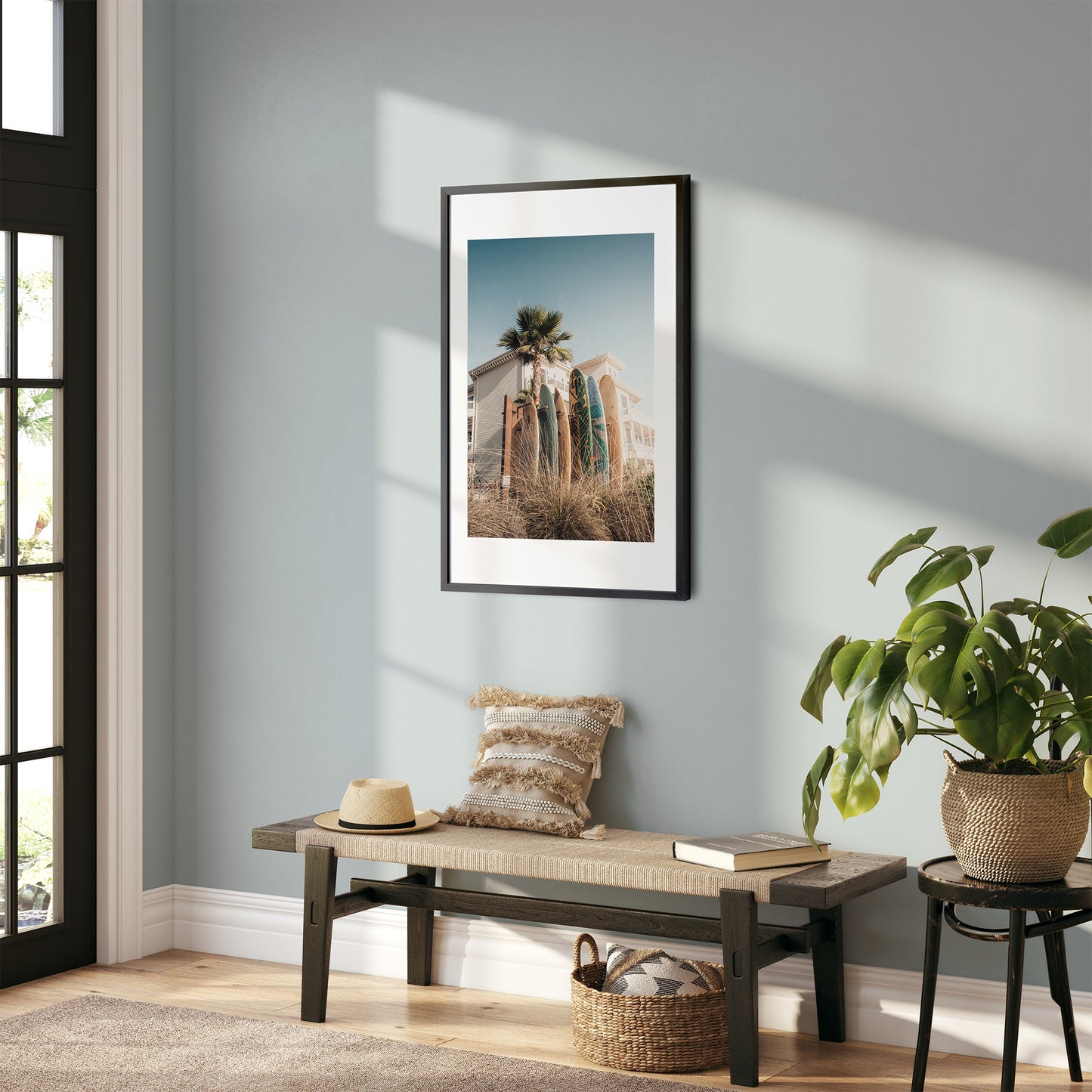 A bright room features a bench with a cushion beneath Coronado Surfboards frame; nearby are a plant and basket on the floor.