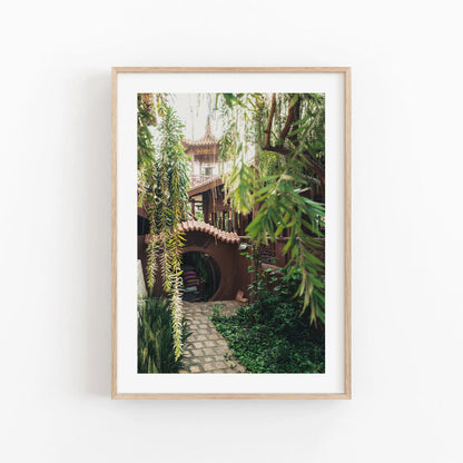 Earthy Enlightenment: Framed photo of a garden path leading to an archway under a treehouse with hanging greenery.