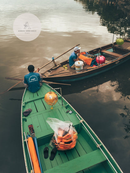 Two people in wooden boats, Evening Shift with food and supplies, glide on a calm river under a cloudy sky.