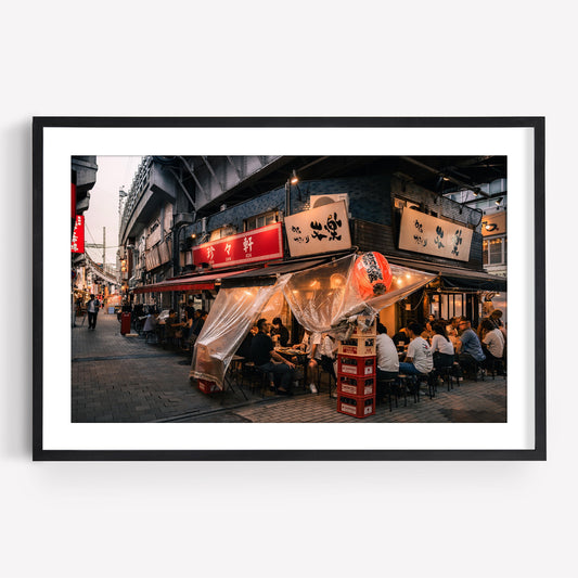 Framed photo, "Flavors Of Ueno": a lively Japanese street restaurant at dusk with diners and glowing lanterns.