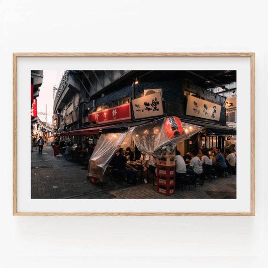 Framed photo titled Flavors Of Ueno depicting a bustling street food stall with diners seated under a canopy along a busy street.