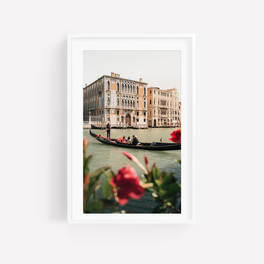 Floral Passion: A gondola glides on a Venetian canal, historic buildings and vibrant red flowers in front.