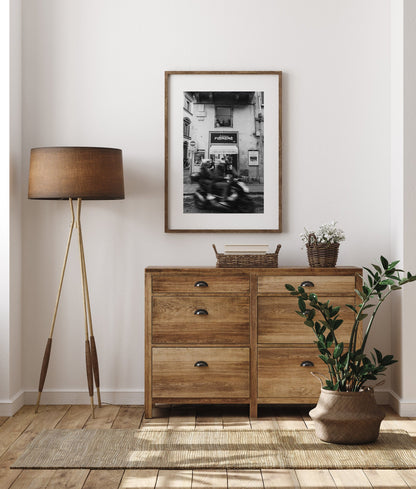 Cozy room with a wooden dresser, Florence Motorcycle art, tripod lamp, potted plant, and woven baskets on wood floor.