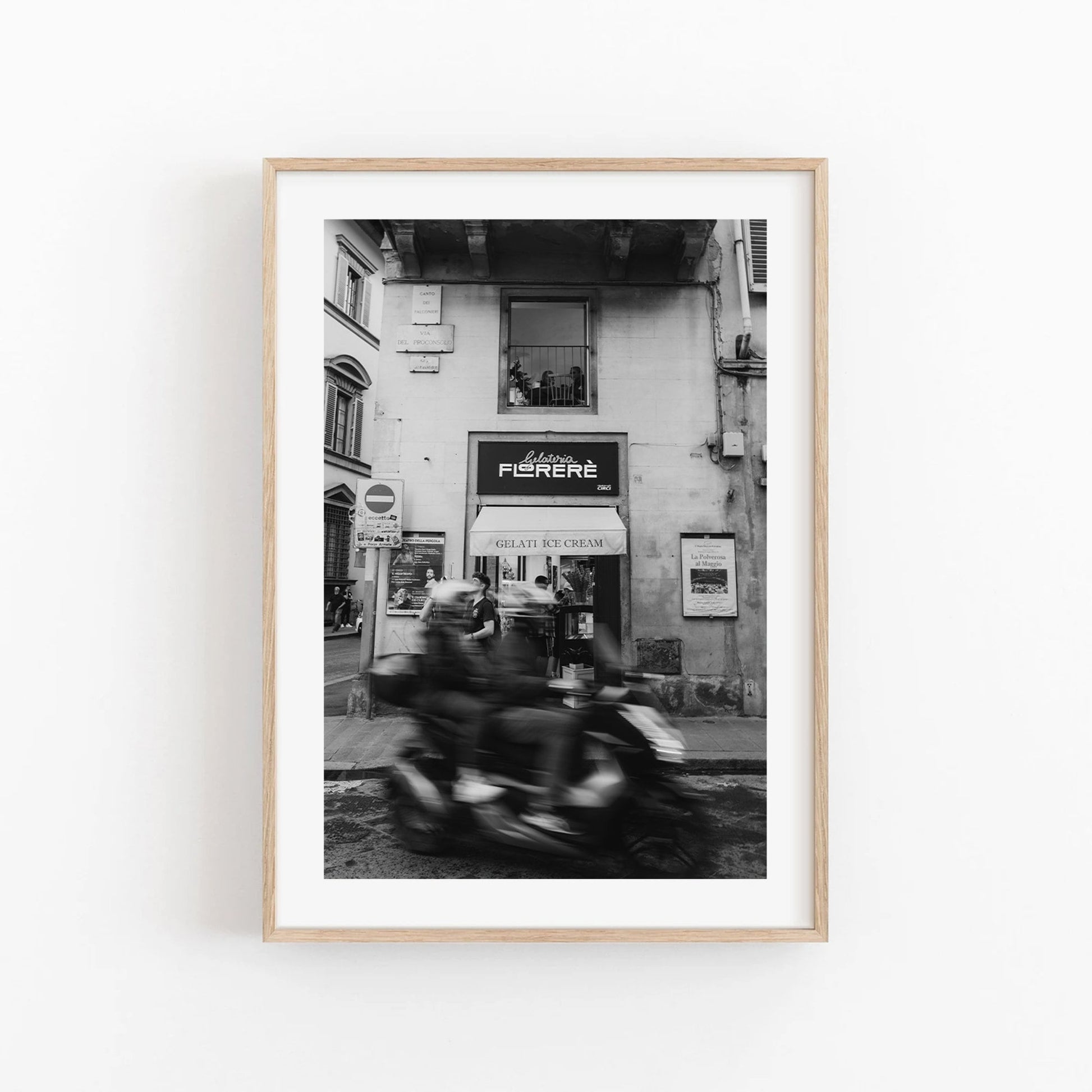 Photo of the Florence Motorcycle in black and white featuring a scooter passing by a gelato shop.