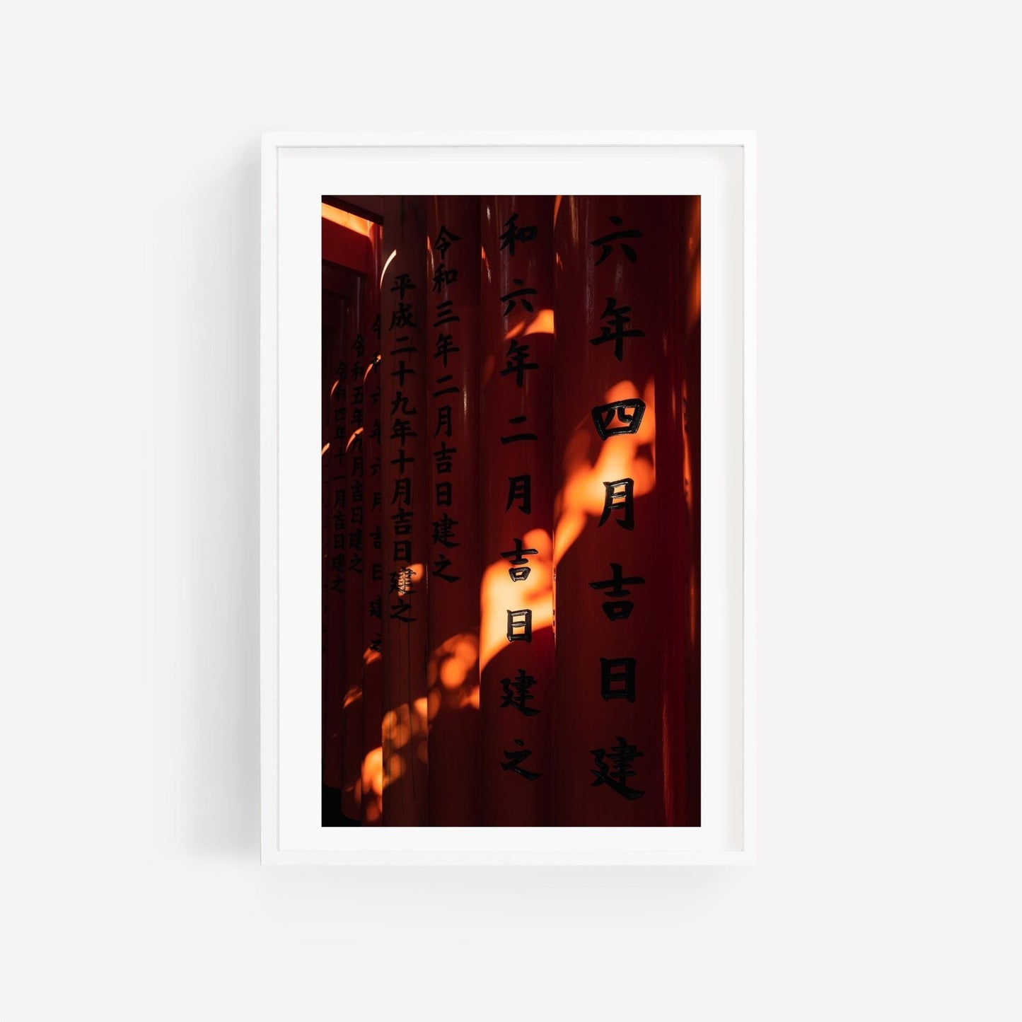 Photography print of Fushimi Inari Taisha red torii gates in a white frame. The intricate inscriptions are illuminated by warm morning shadow.