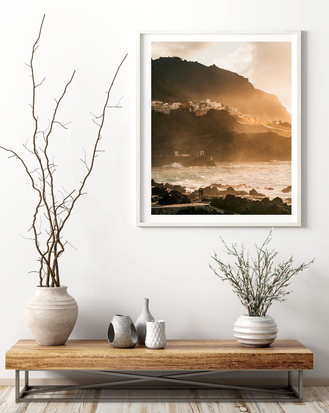 Golden Garachico coastal landscape photo framed above a wooden console with vases and dried minimalist branches.