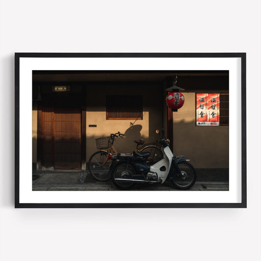 Framed photo titled Golden Shadow featuring a vintage bicycle and scooter against a traditional Japanese building with a red lantern.